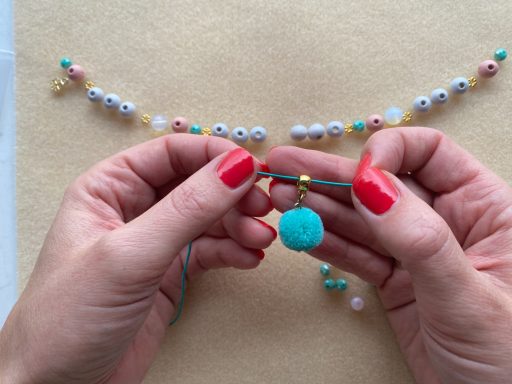 Handen met rode nagellak houden een turquoise kraal en een draad, terwijl ze bewerken.